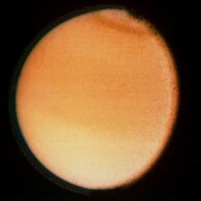 ภาพไททันที่ถ่ายในย่านแสงขาว แสดงถึงโลกที่ปกคลุมไปด้วยเมฆไฮโดรคาร์บอนสีส้มทั่วทั้งดวง (ภาพจาก NASA/JPL)